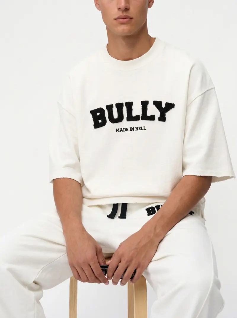 Cream Made In Hell tee and matching sweatpant co-ord, seated on a stool, on an AI male model