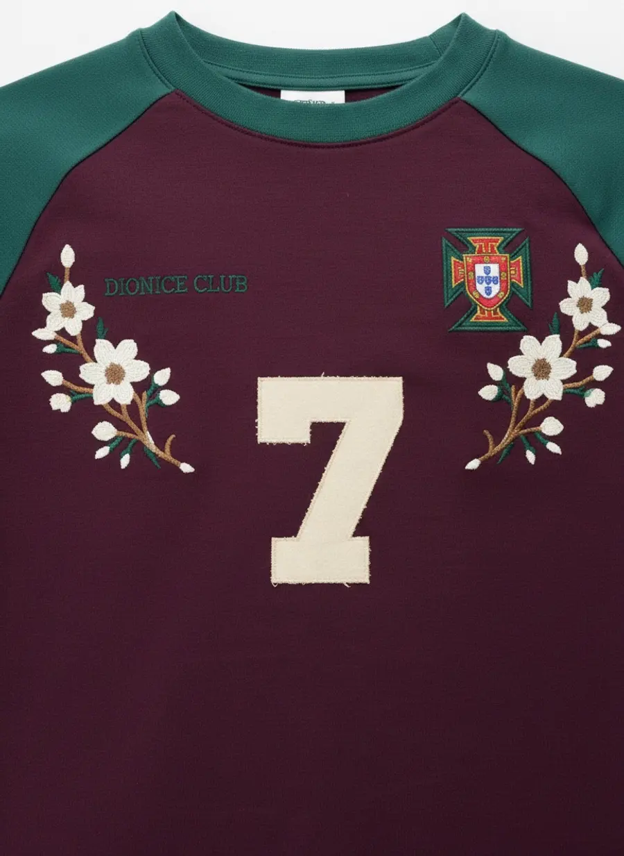 Close up of a plum and cream raglan tee showing an embroidered crest, floral embroidery and an appliqué number seven