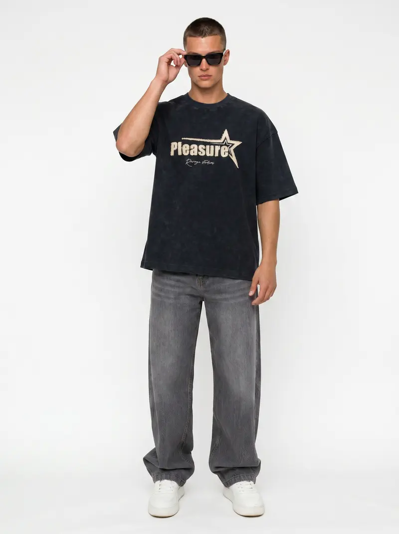 Bully Pleasure Star Tee in black on the same male model in black sunglasses in a white studio, posed differently from the other colourways