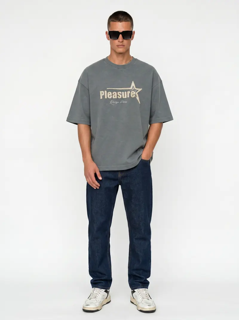 Bully Pleasure Star Tee in sage on the same male model in black sunglasses in a white studio, posed differently from the other colourways