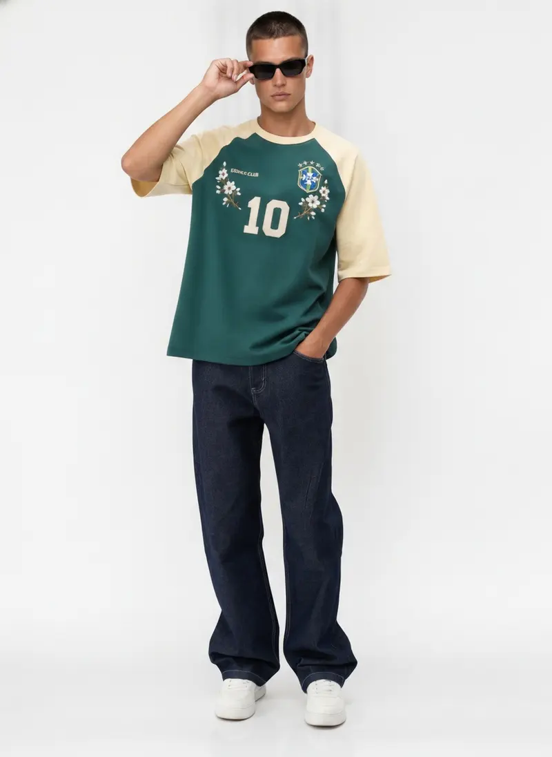 Bully Essence Club Raglan in green / cream on the same male model in black sunglasses in a white studio, posed differently from the other colourways