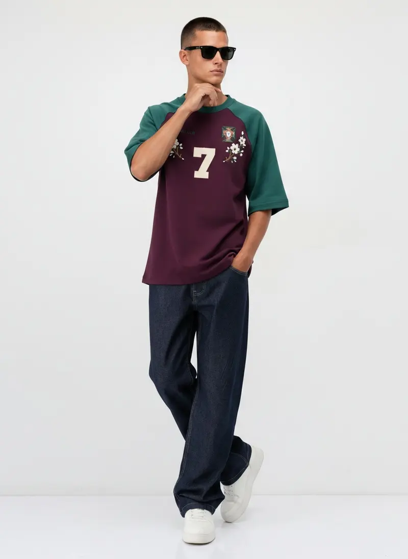Bully Essence Club Raglan in plum / green on the same male model in black sunglasses in a white studio, posed differently from the other colourways