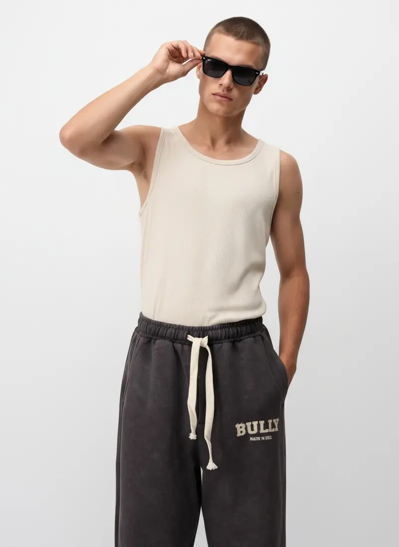 Bully Bully Sweatpant in brown on the same male model in black sunglasses in a white studio, posed differently from the other colourways