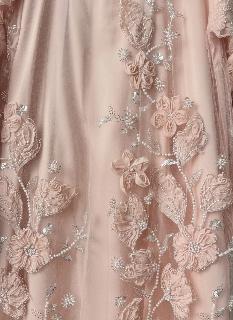 Close-up macro of raised 3D floral appliqué and pearl beading on sheer blush tulle over satin