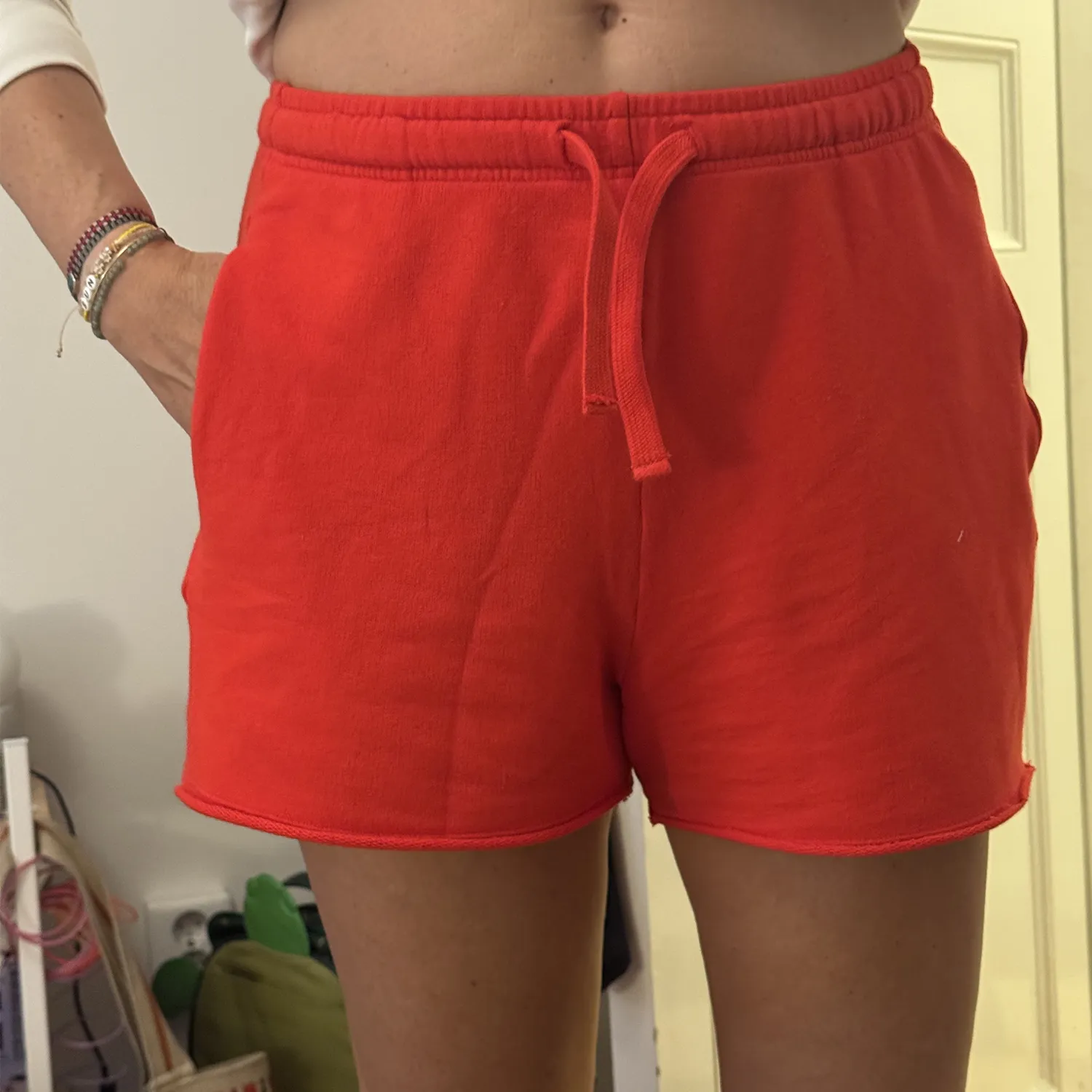 Seller's iPhone photo of red drawstring sweat shorts taken in her bedroom with kitchen and closet visible in the background, the original input for the MODA AI catalog generation