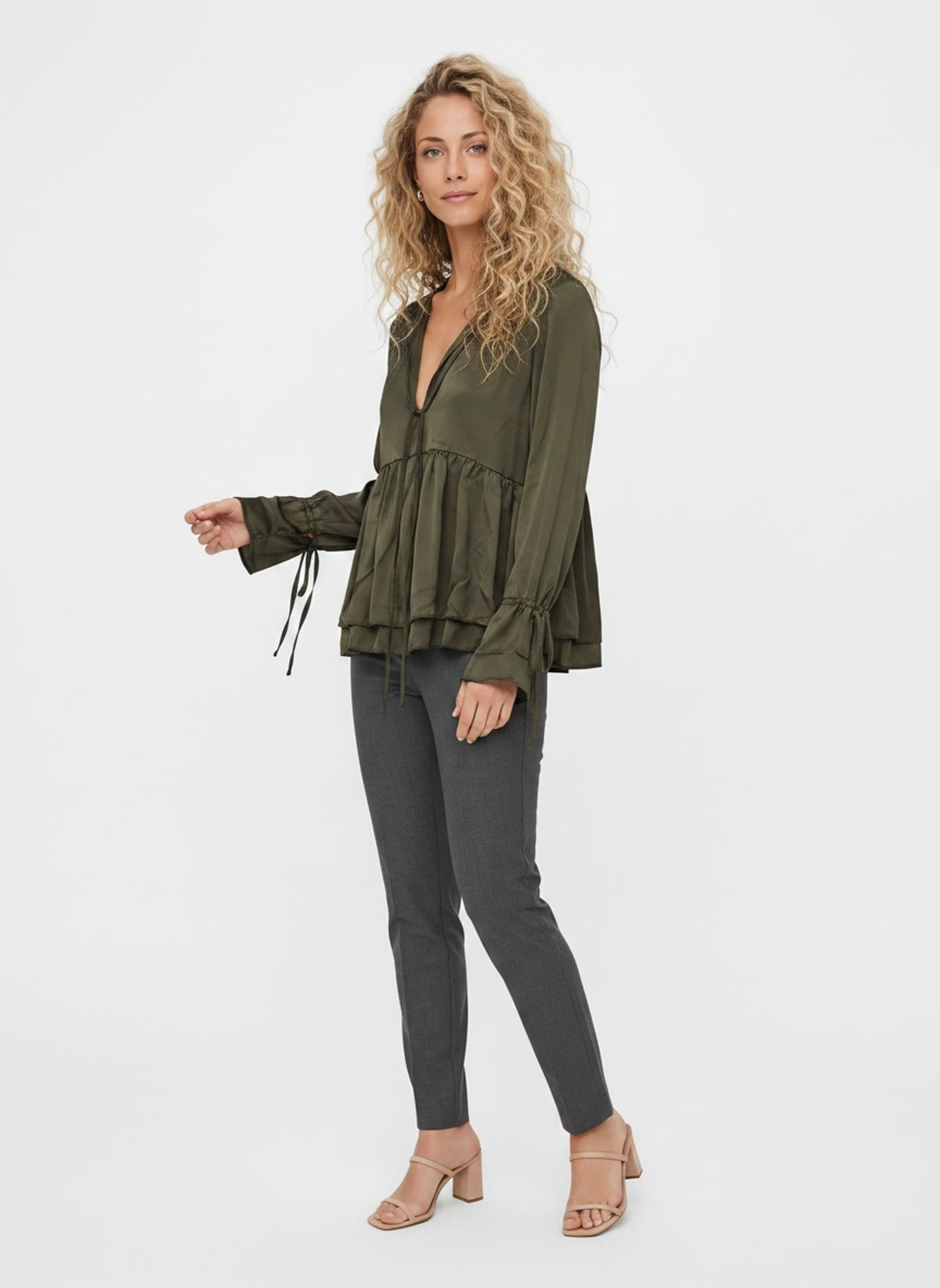 MODA AI output — a woman wearing an olive tiered blouse with grey trousers in a clean studio, generated from a photo of the blouse hanging on a shop wall