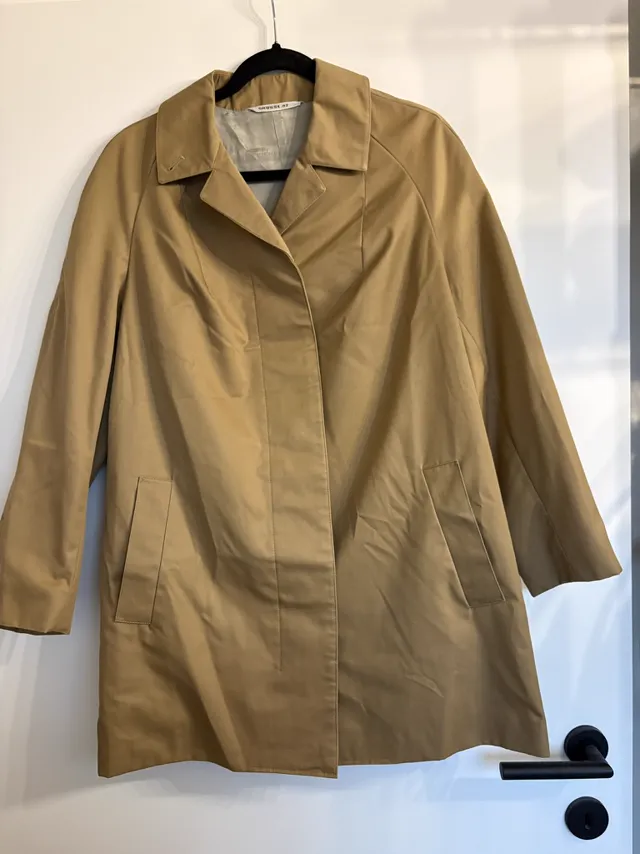 A camel car coat hanging on a hanger against a white door with a black handle, a phone photo used as the input for the coat set