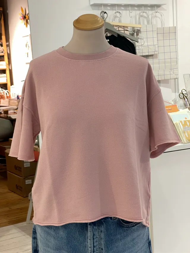 A blush boxy tee on a dress form in a cluttered stockroom, a phone photo used as the input for the tee set