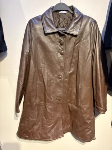 The seller’s phone photo of a brown leather car coat on a hanger against a shop wall, front view