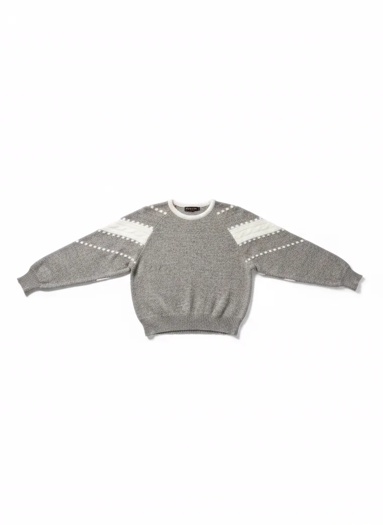A grey marled crew-neck knit with white intarsia stripes and dots down the sleeves and a cream neckline, worn with black trousers. Intarsia Stripe Knit in grey, laid flat