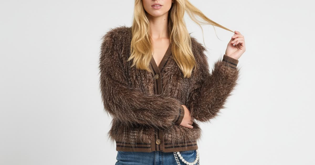A model in a shaggy brown faux-fur jacket with long brown and cream pile, one hand lifting her hair