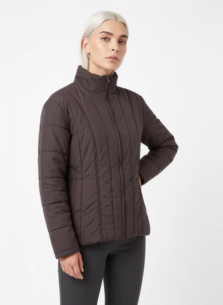 A dark brown channel-quilted puffer jacket with a stand collar and zip front, worn with grey trousers. Channel-Quilted Puffer in dark brown, three-quarter, hand in pocket