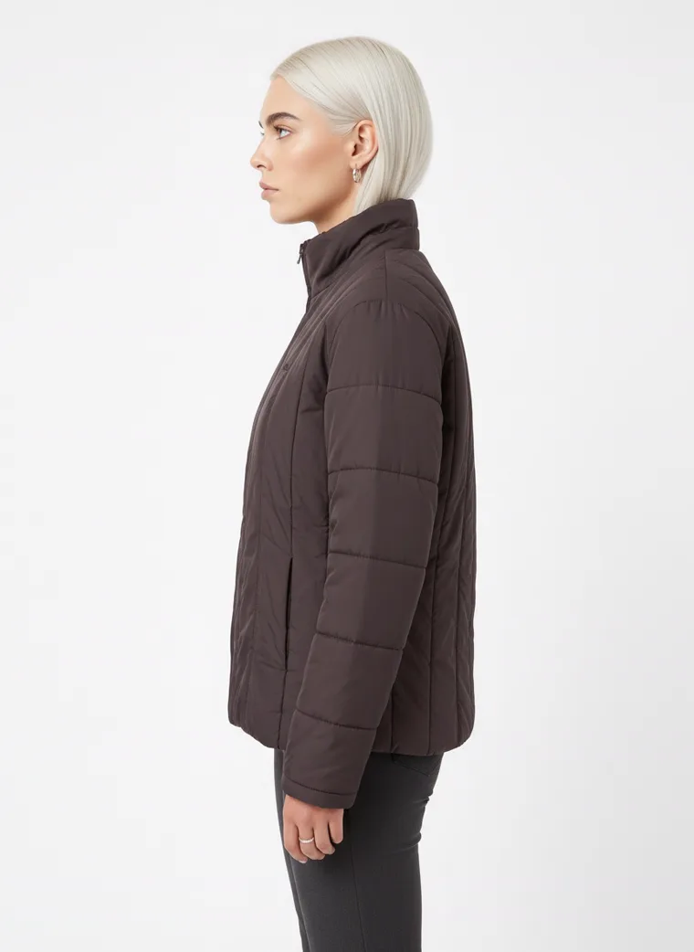 A dark brown channel-quilted puffer jacket with a stand collar and zip front, worn with grey trousers. Channel-Quilted Puffer in dark brown, side view
