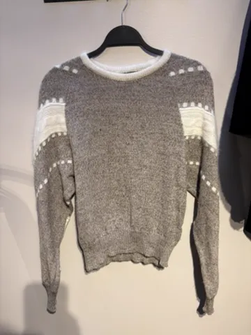 The starting photo for the intarsia stripe knit: the grey intarsia knit on a hanger against a shop wall